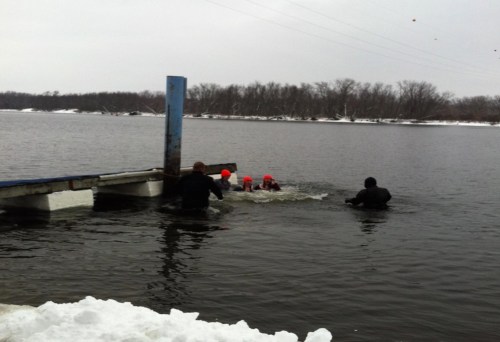 A group of people in bright hats swimming near a dock in a cold, snowy environment.