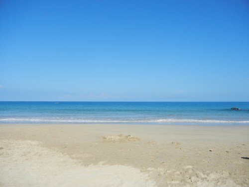 A serene beach scene with clear blue skies, calm ocean waves, and a sandy shore.