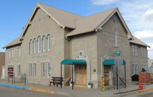 Historic building with a stone facade, arched windows, and a peaked roof, featuring green awnings and a bench outside.