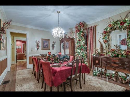 A festive dining room with a red tablecloth, elegant table settings, and holiday decorations, including greenery and ornaments.