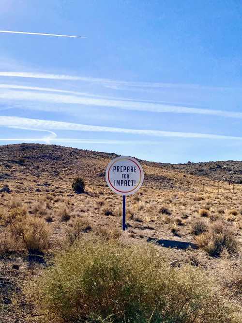 A sign in a desert landscape reads "Prepare for Impact!" against a clear blue sky.