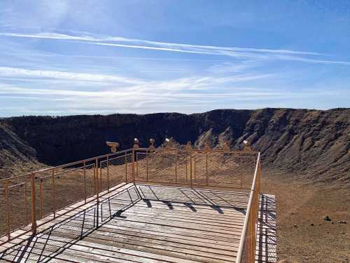 View from a wooden observation deck overlooking a large, dry crater under a clear blue sky.