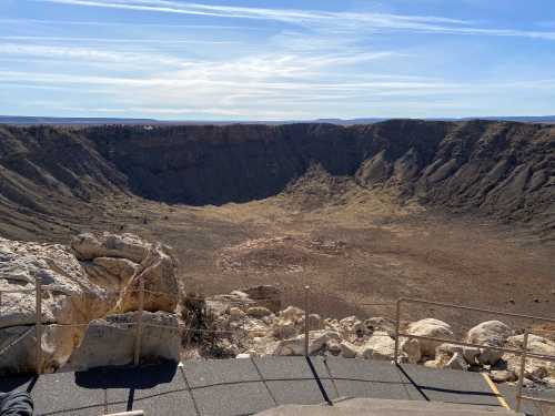 A vast, barren crater surrounded by rocky terrain under a clear blue sky.