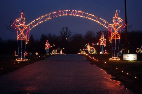 A festive archway of lights featuring toy soldiers welcomes visitors to a holiday display on a dark evening.