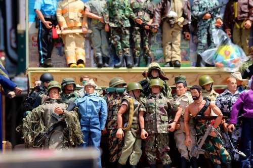 A collection of action figures dressed in various military and civilian outfits, displayed on a wooden shelf.