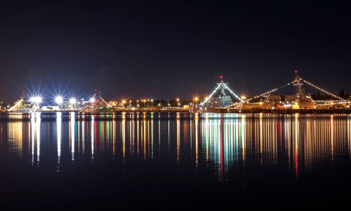 Night view of a waterfront with illuminated bridges and reflections on the water.