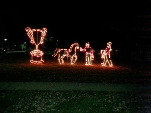 A festive display of lights featuring a trophy, a horse, and a person in winter attire, set against a dark background.