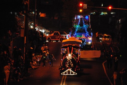 A festive parade at night featuring illuminated floats and a crowd watching along the street.