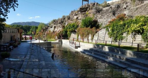 A serene landscape featuring a stone pathway alongside a calm waterway, surrounded by greenery and rocky hills.