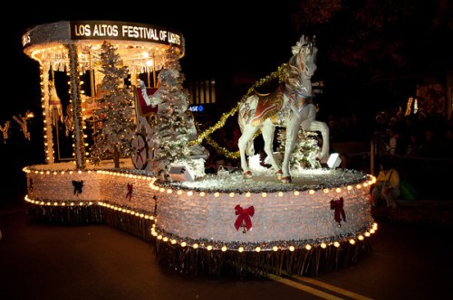 A festive parade float decorated with lights, featuring a white horse and holiday decorations for the Los Altos Festival of Lights.