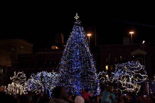 A brightly lit Christmas tree adorned with blue lights, surrounded by festive decorations at night.
