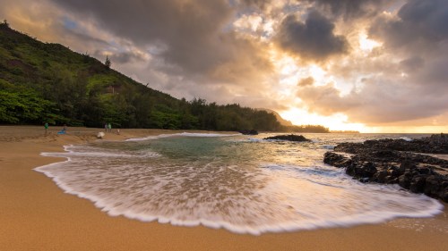 A serene beach at sunset, with gentle waves lapping at the shore and lush greenery in the background.