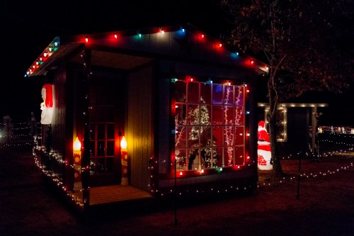 A festive house decorated with colorful lights and Santa figures, set against a dark night sky.