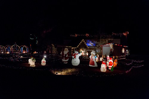 A festive display of colorful Christmas lights and inflatable decorations, including snowmen, Santa, and holiday characters.