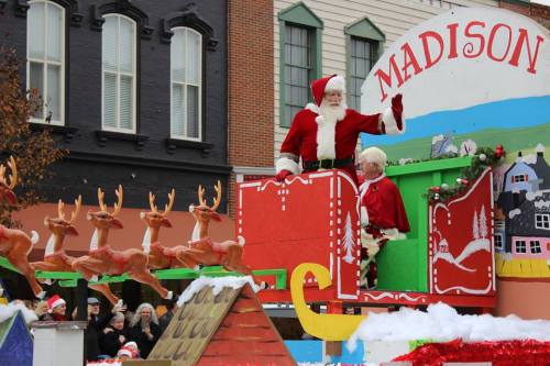 Santa and Mrs. Claus wave from a festive parade float decorated with reindeer and holiday scenes in Madison.