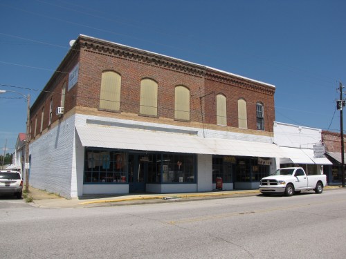 A brick building with boarded windows and a white awning, located on a quiet street with a parked white truck.
