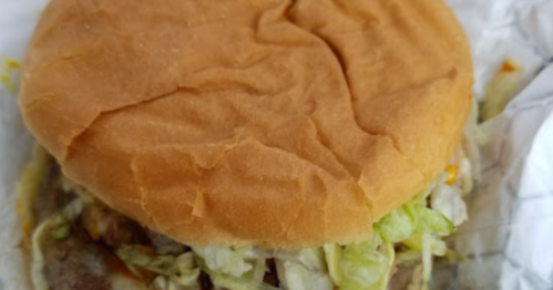 A close-up of a hamburger with a soft bun, lettuce, and a patty, wrapped in paper.