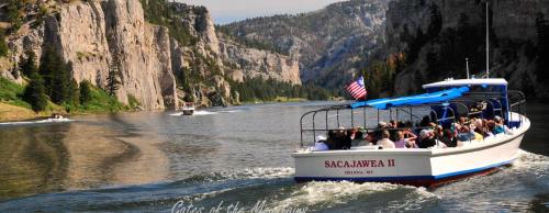 A tour boat named Sacajawea II navigates a scenic river surrounded by cliffs and lush greenery.