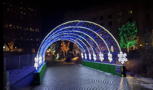A festive archway of blue and white lights with snowflake decorations, set in a winter landscape at night.