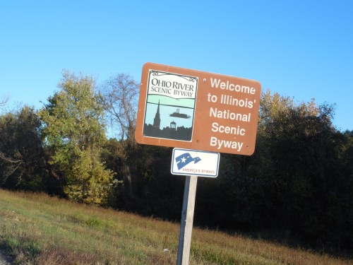 Sign welcoming visitors to the Ohio River Scenic Byway in Illinois, with a clear blue sky and trees in the background.