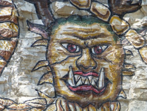 A colorful mural of a fierce creature with sharp teeth and red eyes, painted on a rocky surface.
