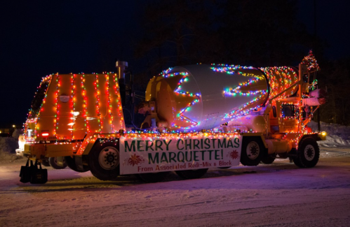 A brightly lit cement mixer truck decorated for Christmas, featuring a festive banner that reads "Merry Christmas Marquette!"