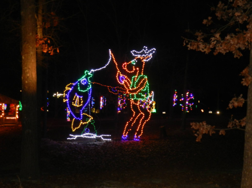 Colorful holiday lights depict a reindeer and a whimsical character in a nighttime forest setting.