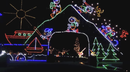 Colorful holiday lights depict a snowy mountain scene with playful figures, trees, and a boat, creating a festive atmosphere.