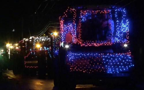 Trucks decorated with colorful lights parade down a street at night, creating a festive atmosphere.