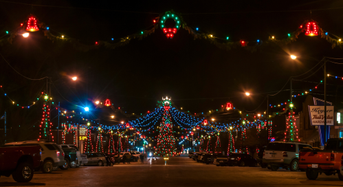 A festive street adorned with colorful lights and a large Christmas tree, creating a cheerful holiday atmosphere at night.