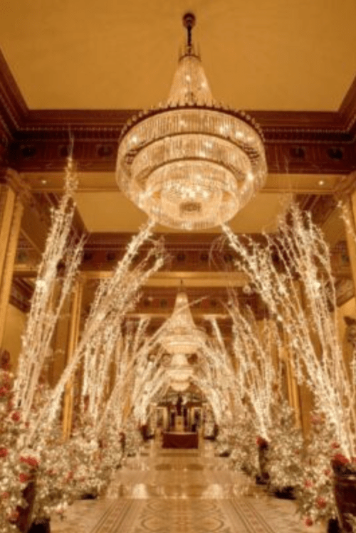 A grand hallway adorned with sparkling lights, chandeliers, and festive decorations, creating a magical holiday atmosphere.