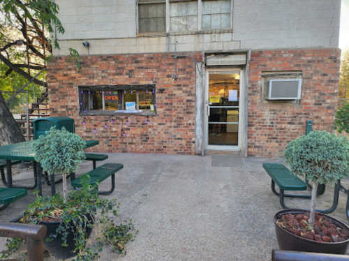 Exterior view of a brick building with an open door, outdoor seating, and potted plants.