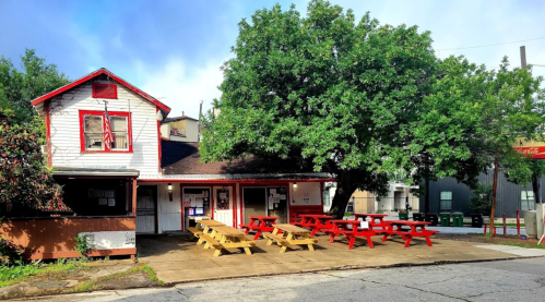 A quaint building with a red and white exterior, featuring picnic tables outside under a large tree.
