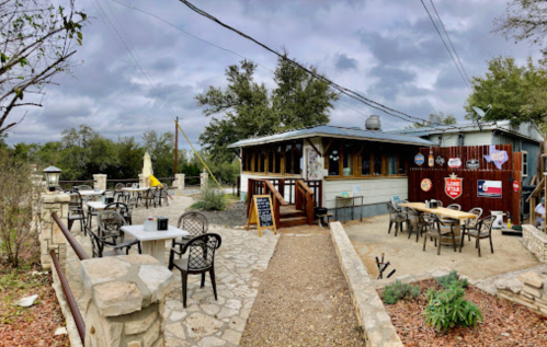A cozy outdoor dining area with stone pathways, tables, and a rustic building under a cloudy sky.