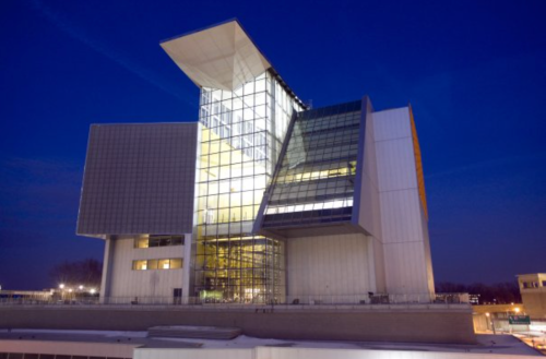 Modern architectural building with large glass panels, illuminated at dusk against a deep blue sky.