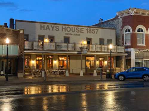 Historic Hays House 1857 restaurant at dusk, featuring outdoor seating and a reflective wet street.