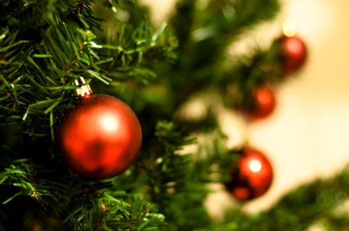 Close-up of a Christmas tree with green branches and red ornaments hanging from it.