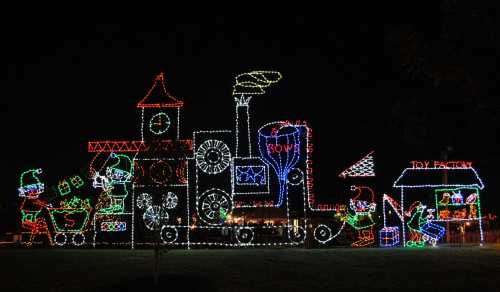 Colorful holiday lights depict a train with elves and a toy factory, set against a dark night sky.