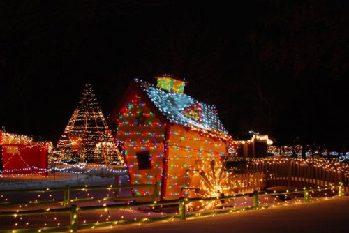 A brightly lit, whimsical house decorated with colorful lights, surrounded by festive trees and glowing decorations at night.