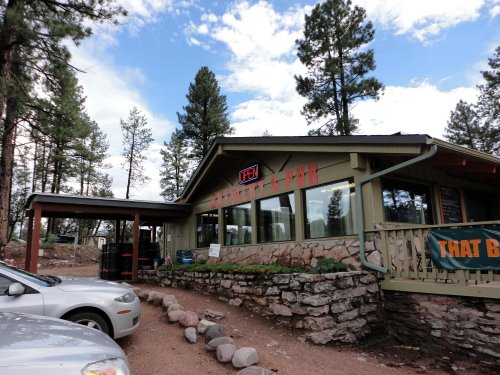 Exterior of a rustic pub surrounded by trees, with a sign reading "PEN" and a parking area in front.