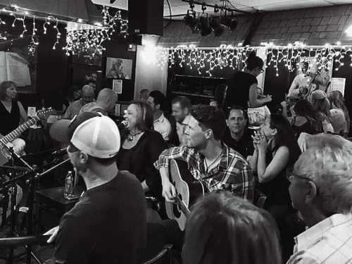 A lively music venue filled with people enjoying a performance, with string lights creating a warm atmosphere.