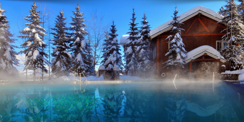 A serene winter scene featuring a steaming pool surrounded by snow-covered trees and a cozy wooden cabin.