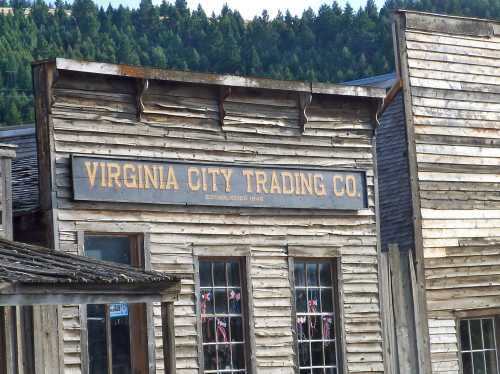 Sign for Virginia City Trading Co. on a rustic wooden building, surrounded by trees in the background.