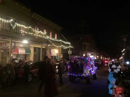 A festive night parade with decorated floats and people in winter attire, surrounded by twinkling lights.