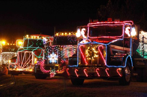Two brightly lit trucks decorated with colorful Christmas lights, parked at night, creating a festive atmosphere.