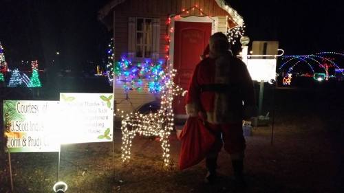 A festive scene with a Santa figure by a decorated house and illuminated reindeer, surrounded by colorful holiday lights.