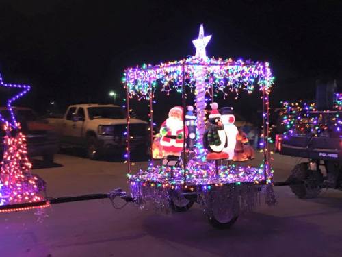 A festive float decorated with colorful lights, featuring Santa and a snowman, set against a dark night sky.