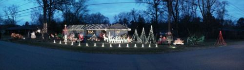 A festive house decorated with colorful Christmas lights, featuring trees, snowmen, and holiday decorations in the yard.