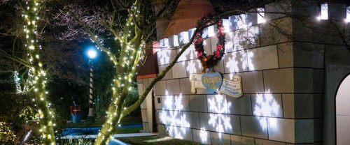 A festive building adorned with holiday lights and decorations, featuring a wreath and snowflake projections.
