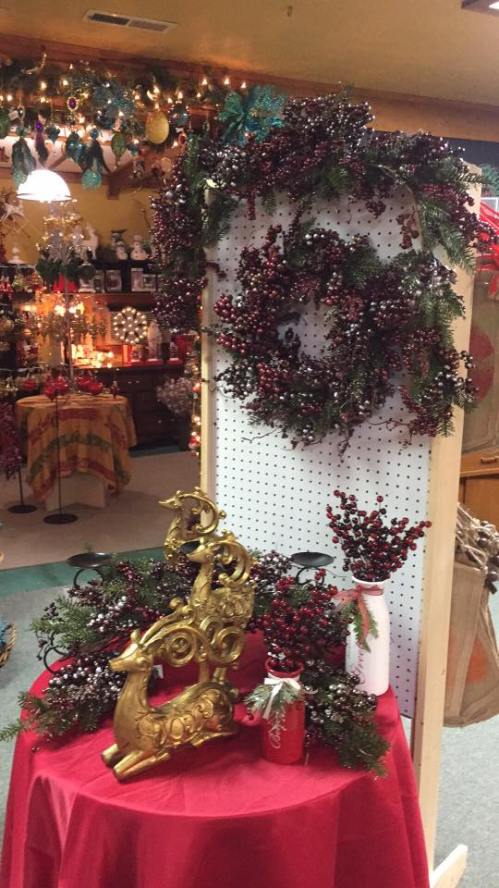 A festive display featuring a berry wreath, decorative branches, and a golden reindeer on a red tablecloth.